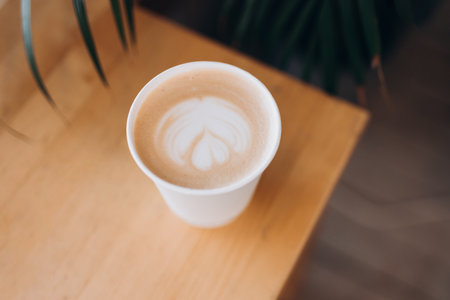 Top view of a paper cup of coffee with latte art on wooden table. Street coffee, top view. Cup coffee in palm branches and leaves. Delicious hot beverage.の写真素材