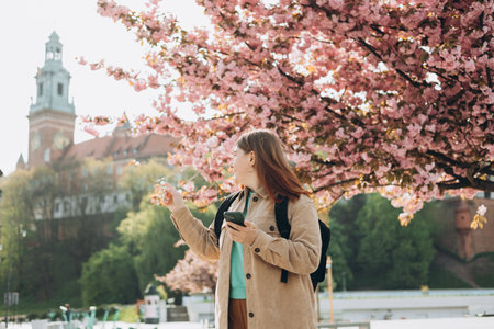 Beautiful stylish woman walking on spring day and holding mobile phone on the street background....