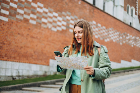 Happy optimistic woman smiling confident holding city map and smartphone at street. Attractive young female tourist is exploring new city. Traveling Europe in spring, old town. Urban lifestyle bannerの写真素材