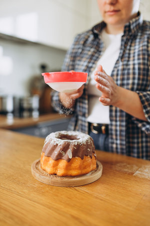 Happy redhead Woman making homemade cake with easy recipe, sprinkling powdered sugar on top. Icing sugar sprinkled with colander. Culinary, baking and cooking food conceptの写真素材