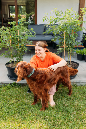 Cheerful happy young woman playing with her dog in the yard of the house in summer. Beautiful Irish...