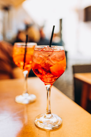 Mezcal Negroni and Spritz Cocktails. Alcoholic beverage based on table with ice cubes outdoors. Served cocktail with orange slice and straw placed on wooden table of sidewalk cafe in Italyの写真素材