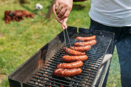 Grilled pork sausage on a cast iron grill. Hand of young woman grilling some meat. Young female having a barbecue, 30s girl preparing food outdoorsの写真素材
