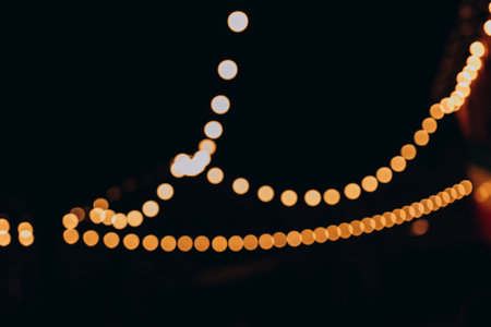 Decorative outdoor string lights at night time, Defocused Background, night city life backdrop, party time with Yellow bokeh ballsの写真素材