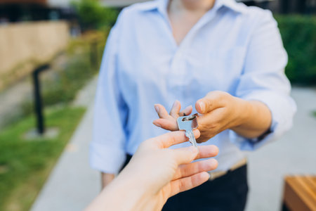Real estate agent giving house keys to woman. Close up of female hand taking house key from realtor....
