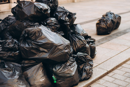Pile of black garbage on the footpath at side road in big city, pollution trash. Many garbage...