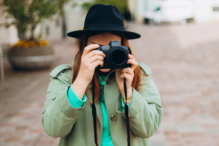 Woman photographer with dcamera taking pictures outdoor. Home hobby, lifestyle, travel, people concept. Portrait of a photographer covering her face with the camera.の写真素材