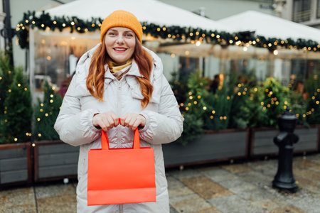 Happy cheerful young Woman holding red shopping paper bags in hands, walking at street. Winter holidays sale. Shopping banner, for mockup, holidays and happiness christmas. High quality photoの写真素材