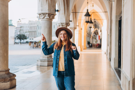 Attractive young female tourist is exploring new city. Redhead girl with backpack pointing finger on city street in Krakow. High quality photo, The Cloth Hall, Vacation conceptの写真素材