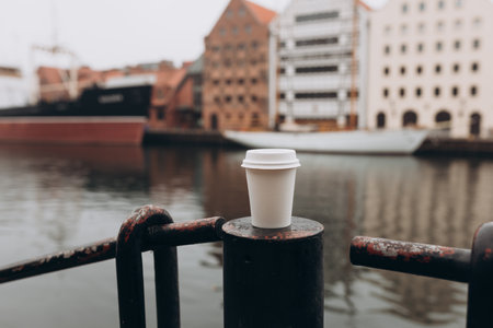 White Paper cup of coffee on bridge near river on city street. Traveling Europe in autumn. Close-up view of disposable paper cup take away, for mockupの写真素材