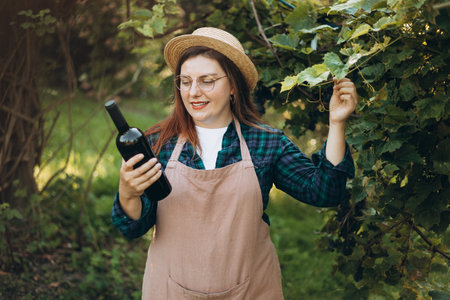 Young happy woman holding a bottle of wine in the grape fields. Ripe grapes in fall. Wine concept