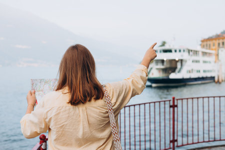 Happy brunette 30s woman enjoying summer holidays. Concept of vacation. Lake Como. Attractive female tourist is exploring new city. Redhead girl holding a paper map and pointing finger on shipの写真素材