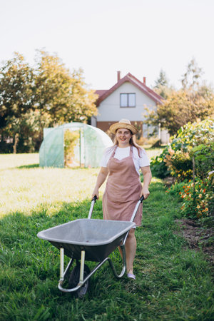 A professional gardener is carrying a wheelbarrow. A young woman with a wheelbarrow is working in the garden, small local farmingの写真素材