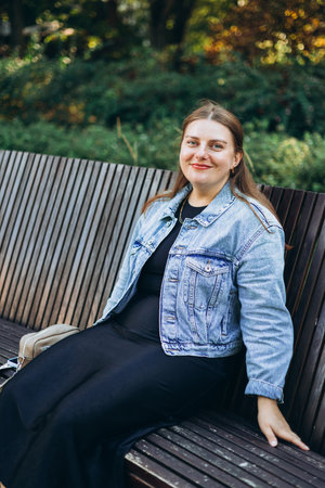 Positive cheerful woman tourist looking at camera on the city street. Happy 30s women relaxing on the bench outdoors. Urban lifestyle concept. Traveler, rest timeの写真素材