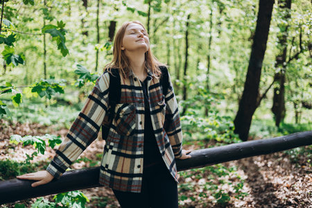 Young happy woman with casual outfit, wears a black backpack walking in the forest. Spring time. 30s...