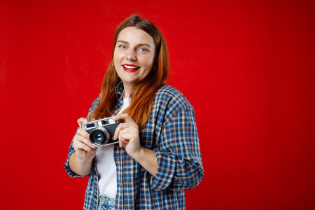 Portrait of a smiling young woman standing with photo camera isolated over red background. Home...