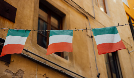 Typical street with houses in Italy. Facade of a yellow building with Italian flags. Italian flags in an old town narrow street of a city in Italyの写真素材