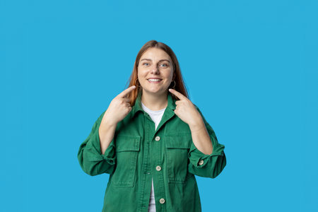 Beautiful young 30s woman pointing finger to her teeth on isolated blue background. Facial and skin...