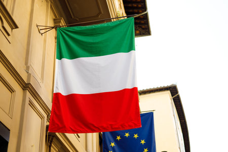 Flag of Italy with EU flag hanging on the wall of a house. Flags in the facade of old buildingの写真素材