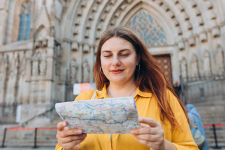 Young woman tourist with paper map standing in front of the famous saint Eulalia church in...