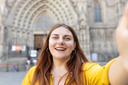 Smiling young woman taking a selfie in front of the famous saint Eulalia church in Barcelona....