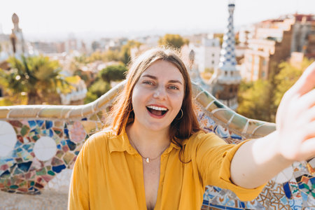 Beautiful female in Gaudi garden, Spain, Barcelona. Young traveling woman taking selfie outdoors. Concept of travel, tourism and vacationの写真素材