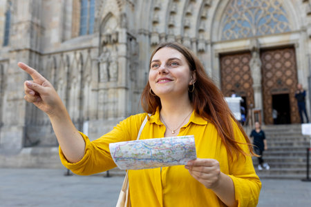 Young woman tourist with paper map standing in front of the famous saint Eulalia church in Barcelona...