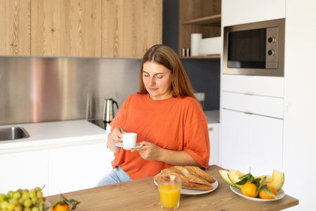 Carefree casual young beautiful happy smiling woman drinking coffee in lazy morning at comfy home interior. Young woman enjoying fresh aromatic coffee in modern kitchenの写真素材