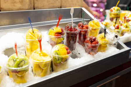 Fruit Salad arranged in plastic cups on a market. Cut and ready fruit ready to sell in market. Convenience, healthy lifestyle. Strawberries, kiwi, garnet, pineapple, coconut in a plastic glass to goの写真素材