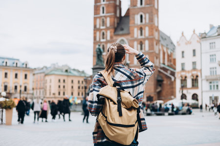 Tourist happy woman posing on Market Square in Krakow, Traveling Europe in autumn. St. Marys Basilica, no face, rear viewの写真素材