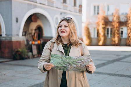Happy young woman with map in old town. Holidays and tourism concept. Female tourist searching...