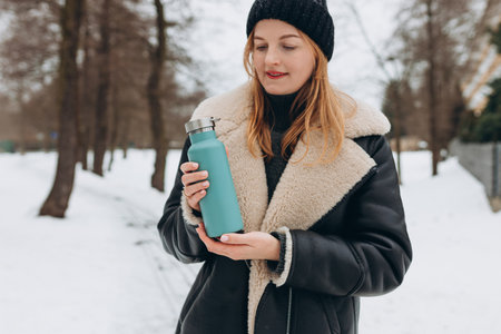 Portrait of a beautiful young woman with bottle in a winter park. Healthy life style, happiness and drink conceptの写真素材