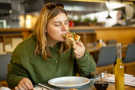 A happy 30s woman holds a piece of pizza in hands. Pizza with prosciutto, ham, arugula, tomatoes and parmesan. Italian cuisine. Food bannerの写真素材