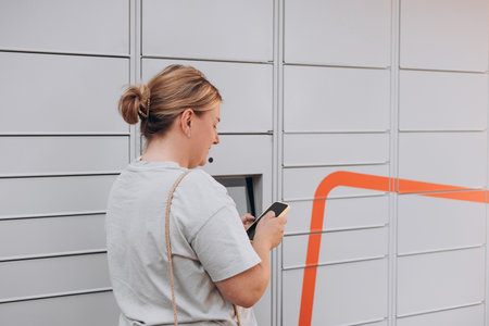 Person using phone at outdoor automated parcel machine. Electronic locker for storing parcels.