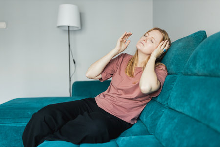 Depressed young woman sitting on couch in the living room at home, Frustrated confused female feels unhappy problem in personal life. Exhausted girl portrait suffering migraine. Hand on head.の写真素材
