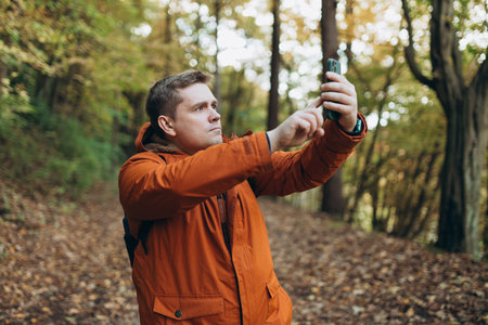Sad angry blonde man got lost and could not find an internet connection on phone while hiking alone in the forest. Road trip, transport, travel, technology and people concept. High quality photoの写真素材