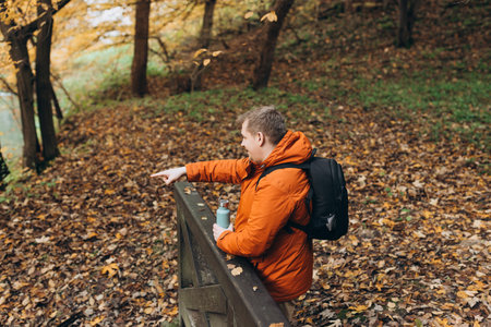 Male with bottle of coffee pointing finger outdoors, he hiking on woodland, rear view. Active...