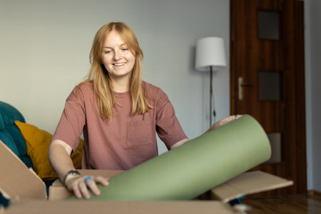 Young cheerful woman in glasses getting parcel at home. Pretty girl sitting on sofa at home and...