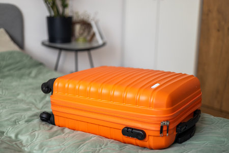 Big orange suitcase on the bed in light room. Baggage case packing getting ready to travel trip vacation. Lifestyle, adventure and tourism concept.の写真素材