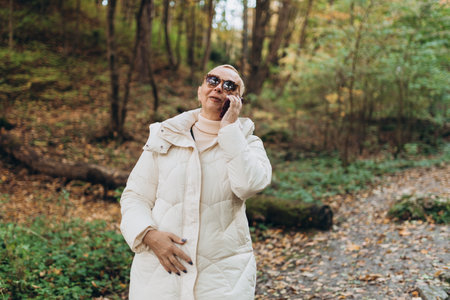 50s woman tourist using smartphone outdoors. Senior female hiking on the road in nature. Beautiful blonde woman walking on autumn landscape. Travel, technology and people banner. High quality photoの写真素材