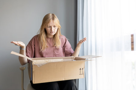 Unhappy young blonde woman frustrated by wrong order shopping online. Upset female buyer unbox parcel buying on web confused with bad delivery service. Shipping conceptの写真素材