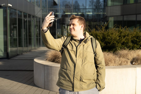 Portrait young man taking selfie on urban background. 30s man using phone outdoors. Smiling man...