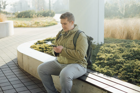 Handsome young man using phone outdoor. Smiling businessman walking outdoors using mobile in urban area. Urban lifestyle concept. Spring time.の写真素材