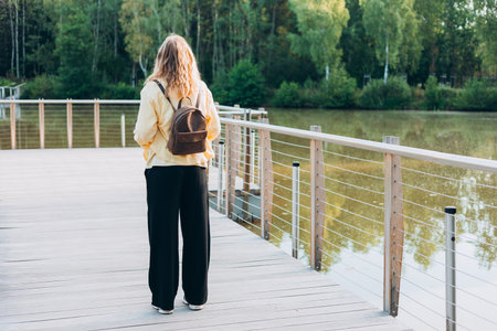 A young happy blonde woman standing on a bridge near a lake on a sunny day. Beautiful morning relax, Full bodyの写真素材