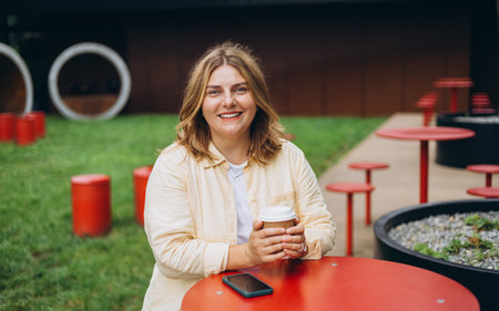 Happy 30s blonde woman enjoying her cup of cappuccino outdoors in cafe, weekend mood. Urban lifestyle concept.の写真素材