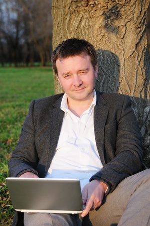 Businessman with laptop working under a tree の写真素材