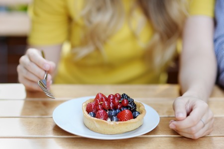 Young woman having custard fruit tart in the outdoors cafeの写真素材