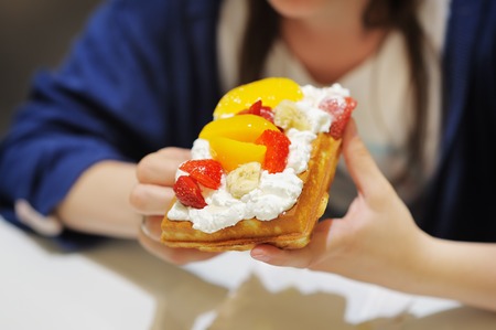 Young woman holding appetizing Belgian waffles with whipped cream and fruitの写真素材