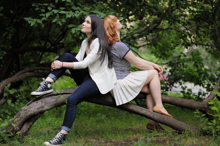 Two beautiful young woman sitting on the treeの写真素材
