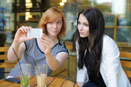 Two young girls taking a self portrait (selfie) with smart phoneの写真素材